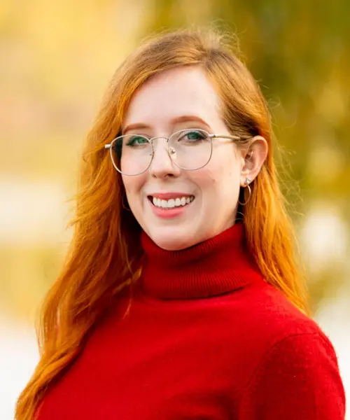 Head Shot of a young woman with long red hair and glasses smiling